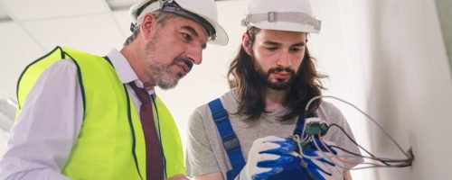 Builder or foreman in working uniform expertising the structure standing with folder at the construction site indoors